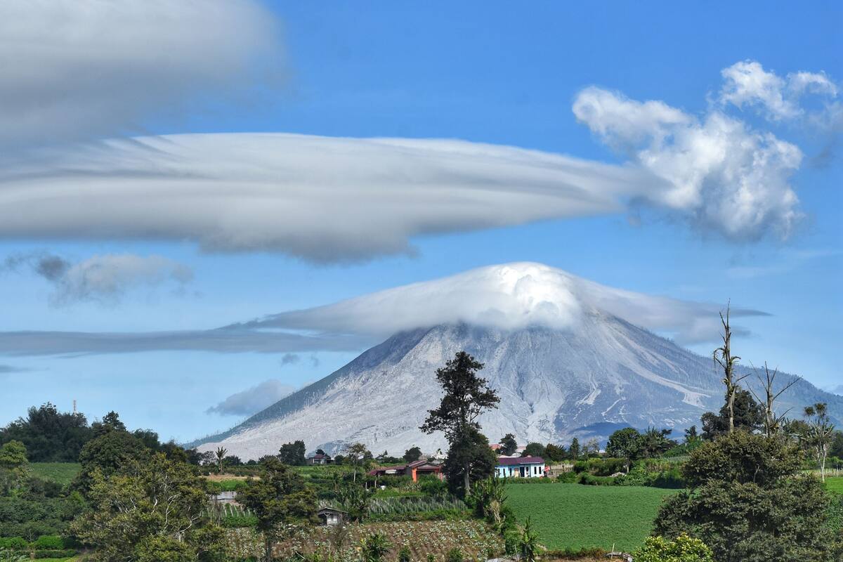 A mountain with a small village at its base, surrounded by greenery and clear skies.