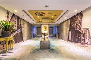 Un vestíbulo de hotel con piso de mármol, una columna central con un jarrón y murales en las paredes.