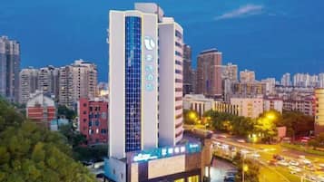 A high-rise hotel with a prominent vertical sign, surrounded by a cityscape at dusk.