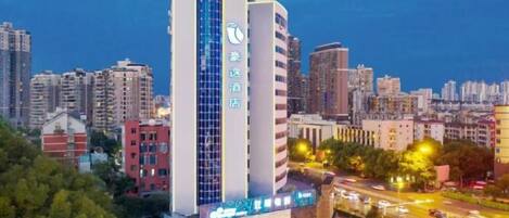 A high-rise hotel with a prominent vertical sign, surrounded by a cityscape at dusk.
