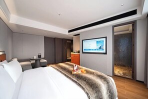 A modern hotel room with a large bed, a small table with a tray of breakfast items, a TV mounted on the wall, and a view of the city through a glass door. - Haoyi Hotel (Zhuzhou)