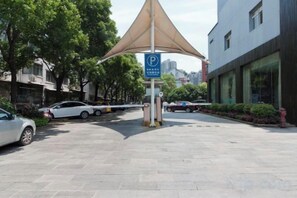 Un área de estacionamiento con marquesina, un letrero de estacionamiento azul y un edificio con amplias ventanas.