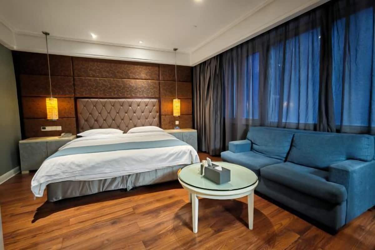 A hotel room with a large bed, a sofa, a glass coffee table, and a view of the night sky.