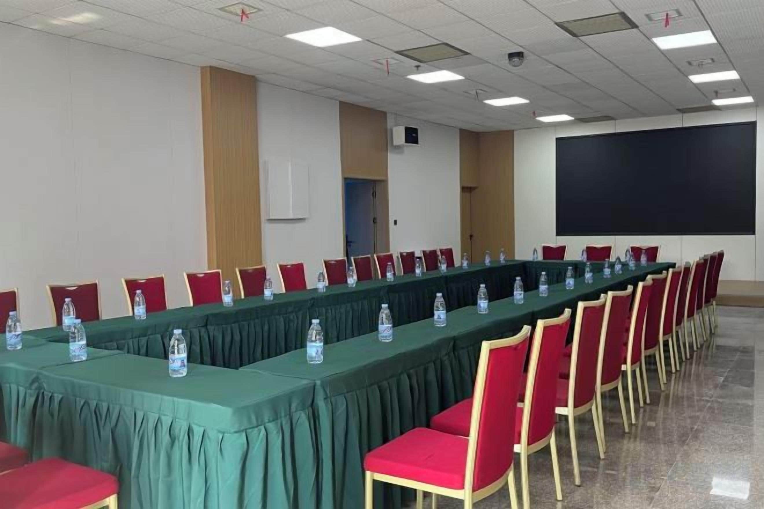 A conference room with a long table, red chairs, and a projector screen.
