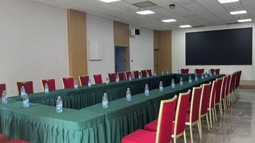 A conference room with a long table, red chairs, and a projector screen.