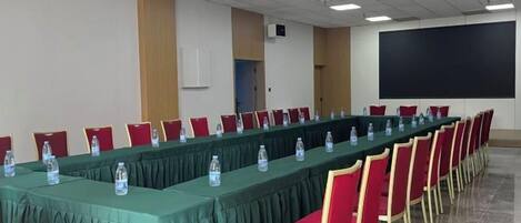 A conference room with a long table, red chairs, and a projector screen.