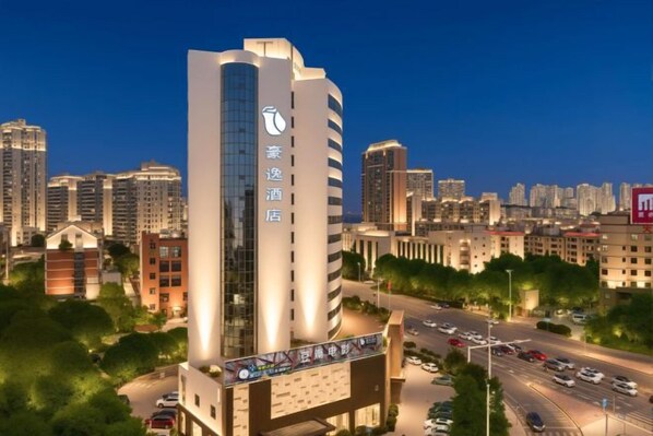 A high-rise hotel with a prominent glass facade, surrounded by a cityscape with other buildings. - Haoyi Hotel (Zhuzhou)