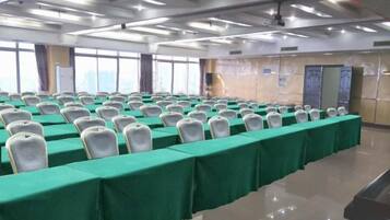 Un salón de conferencias con filas de sillas blancas, manteles verdes y un amplio ventanal.