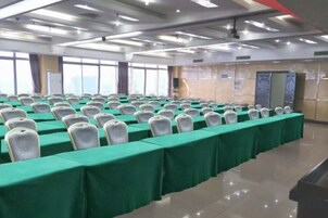 Un salón de conferencias con filas de sillas blancas, manteles verdes y un amplio ventanal.