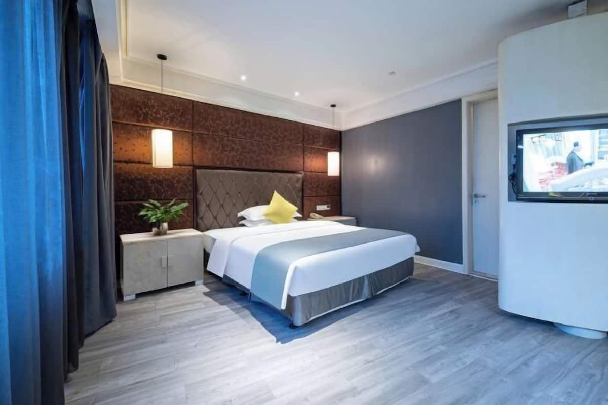 A modern hotel room with a bed, bedside tables, a TV, and a view of the street.