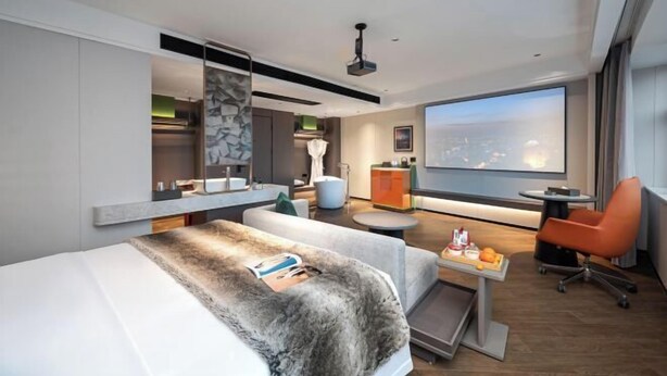 A modern hotel room with a bed, a desk, a chair, a large window with a city view, and a flat-screen TV. - Haoyi Hotel (Zhuzhou)