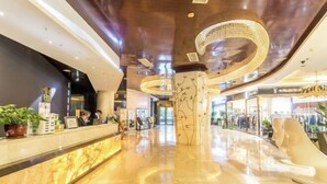 A modern lobby with a marble reception desk, a chandelier, and a curved ceiling design. - Haoyi Hotel (Zhuzhou)