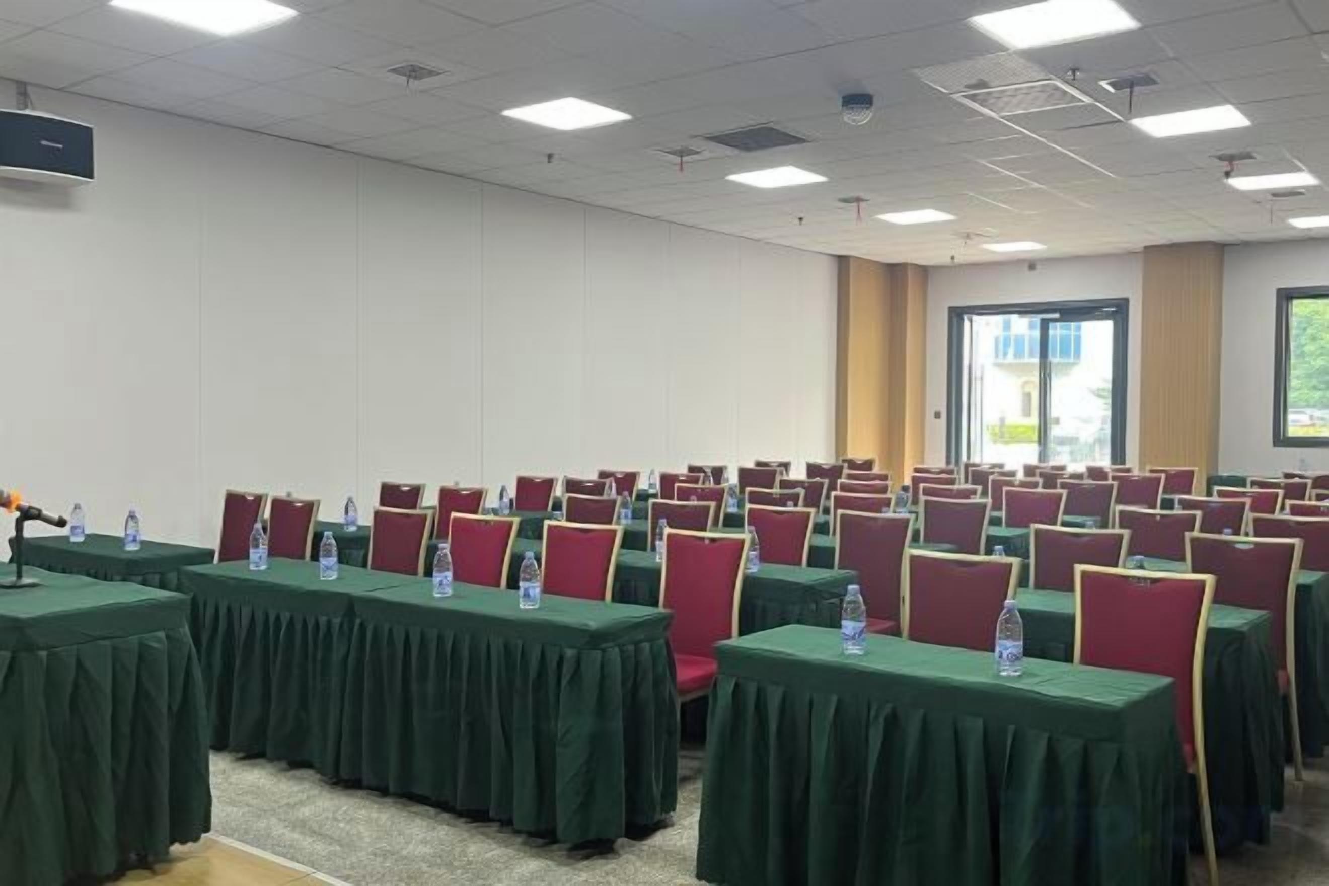 Konferenssihuone, jossa on riveissä pöytiä ja tuoleja, ja jossa on myös vesipulloja.
