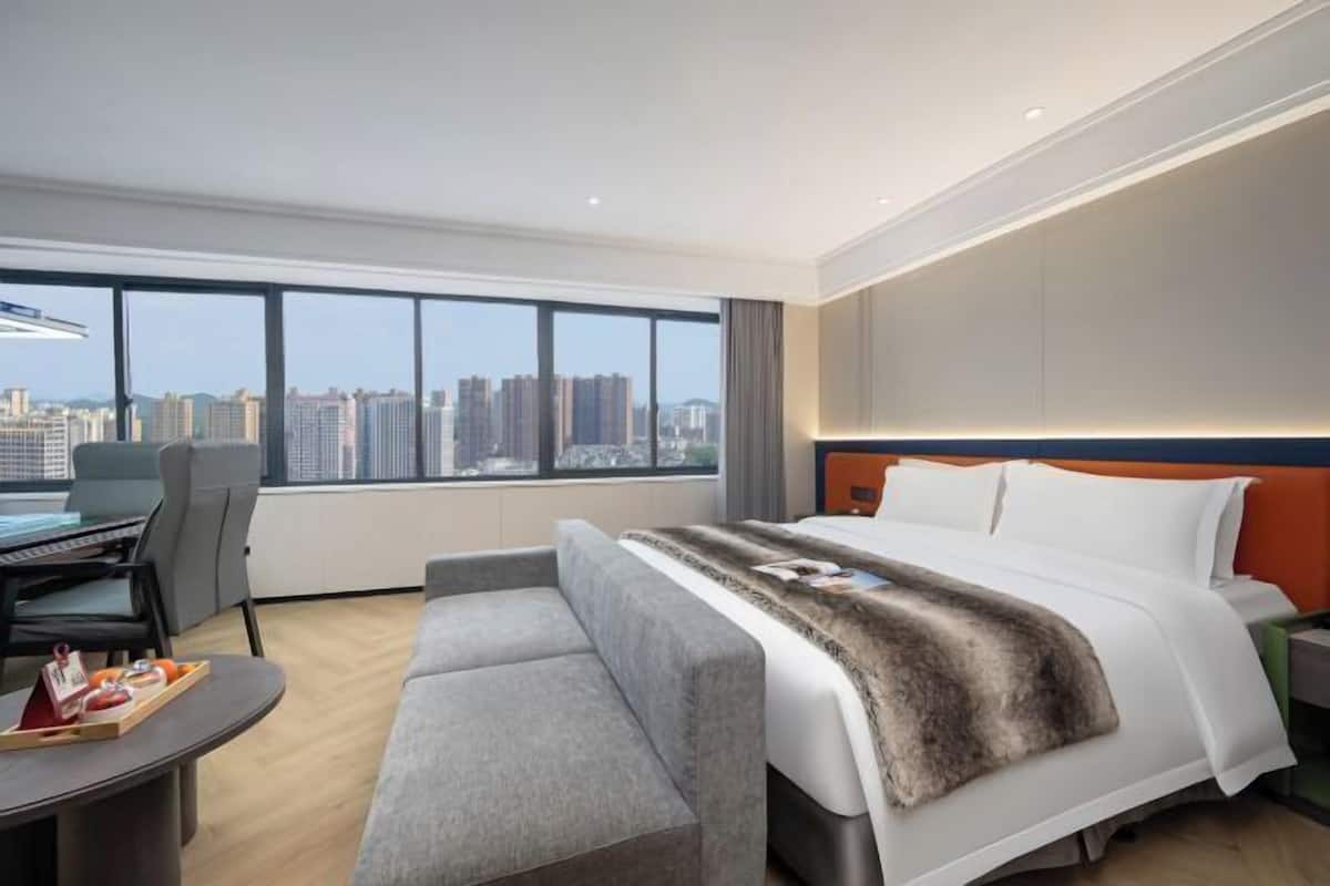 A modern hotel room with a large bed, a desk, and a view of the city skyline.