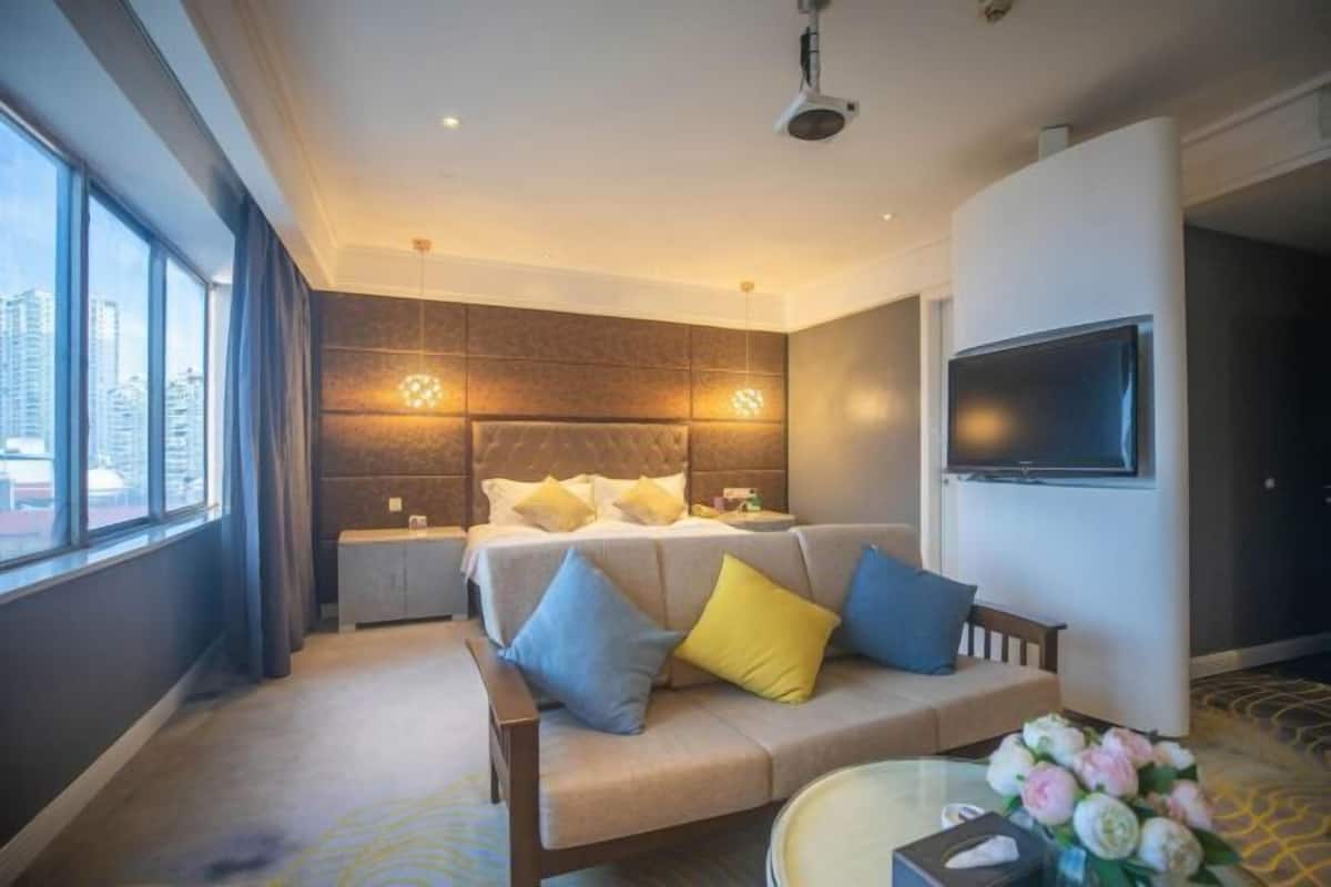 A hotel room with a bed, a sofa, a TV, and a large window.
