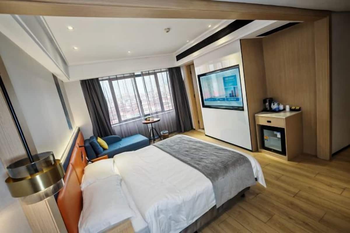 A modern hotel room with a large bed, a desk, a TV, and a view of the city.
