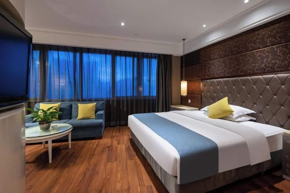 A hotel room with a large bed, a sofa, a small table, and a TV.