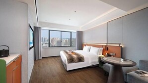 A modern hotel room with a large bed, a desk, a round table, and a view of the cityscape. - Haoyi Hotel (Zhuzhou)