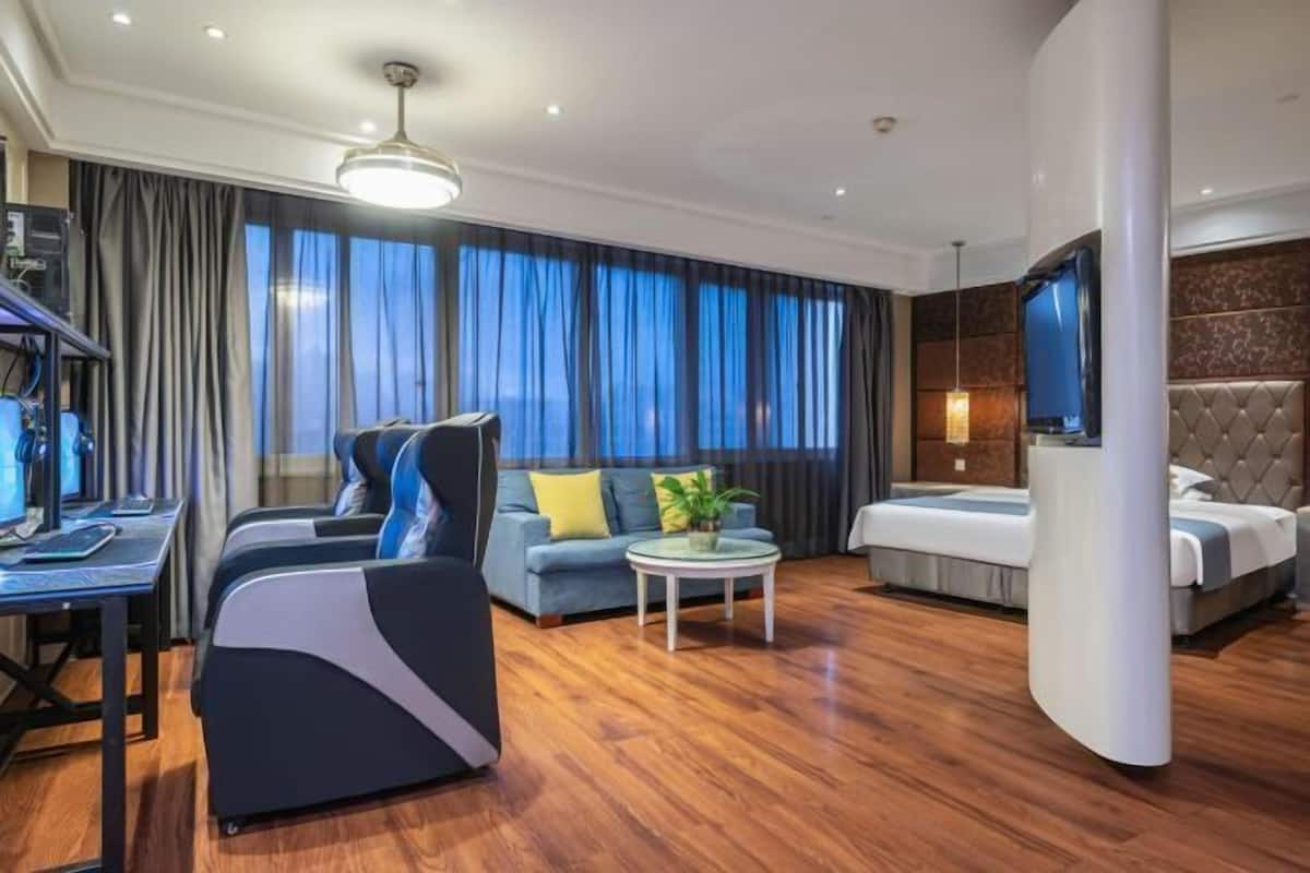 A modern hotel room with a sofa, a bed, a desk with a computer, and a TV.