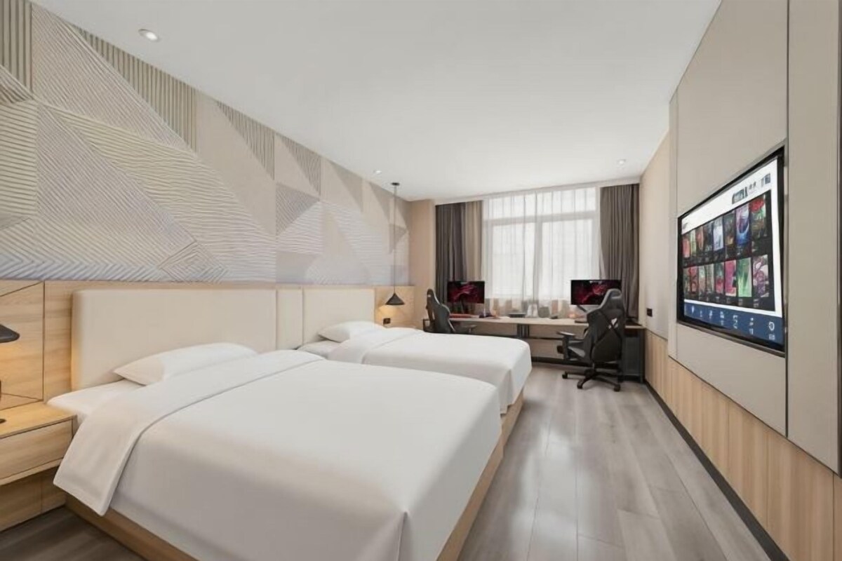 Een hotelkamer met twee bedden, een bureau, een stoel, een televisie en een wandgemonteerd scherm.