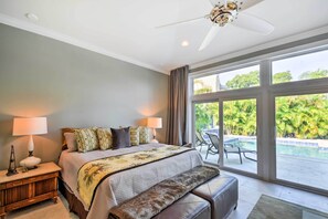 A bedroom with a bed, bedside lamps, a bench, and a view of a pool and greenery. - Expansive St Pete Beach Home: Pool, Walk to Beach (St Pete Beach)