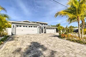 A modern two-story house with a driveway leading to a garage, surrounded by palm trees and a well-maintained garden. - Expansive St Pete Beach Home: Pool, Walk to Beach (St Pete Beach)
