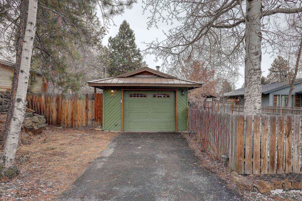 A green garage with a metal roof, surrounded by a wooden fence and trees.