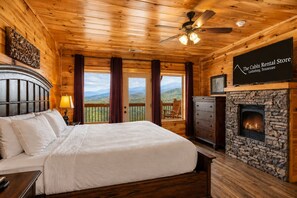 Ein Schlafzimmer einer Hütte mit Bett, Kommode, Kamin, Deckenventilator und Blick auf die Berge.