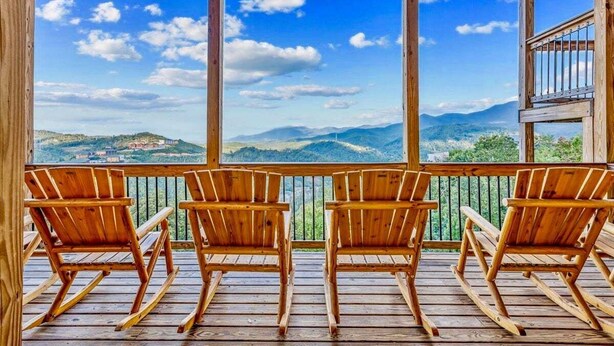 A wooden deck with four rocking chairs facing a scenic mountain view.