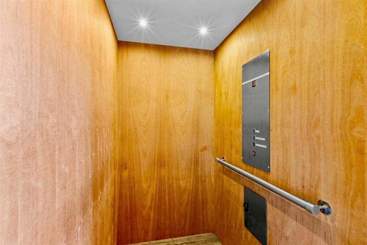 A wooden interior with a metal elevator door, a handrail, and a ceiling light fixture.