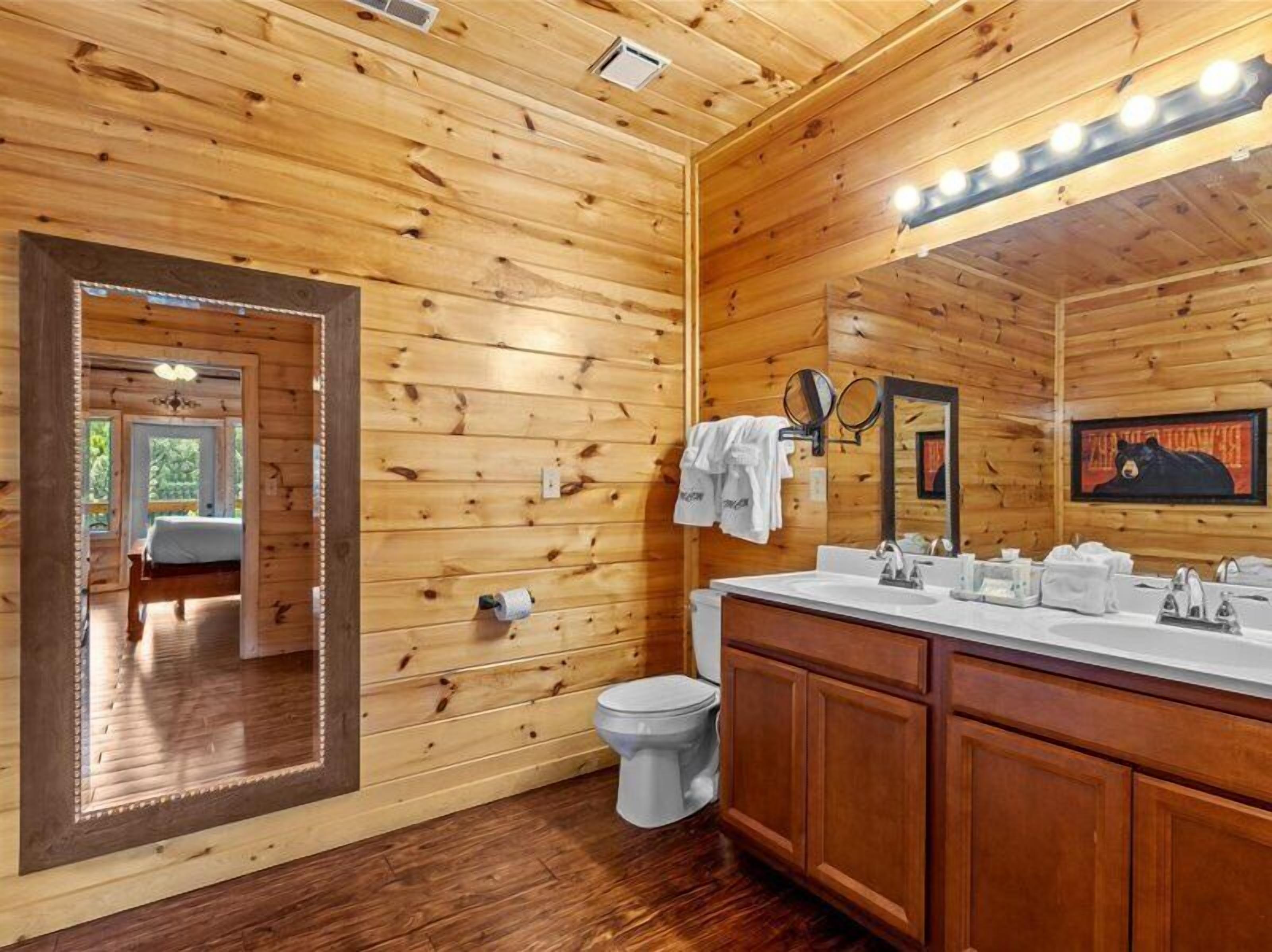 Puisesta mökistä inspiroitunut kylpyhuone, jossa on suuri peili, kaksi pesuallasta ja wc.