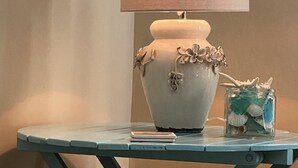 Una mesa con una lámpara, un jarrón con caracolas y un cuaderno.