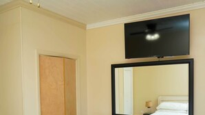 Een slaapkamer met een plafondventilator, een tv boven een dressoir en een bed met een witte dekbedovertrek.