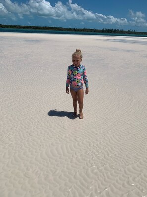 A child walking on a sandy beach with a clear sky and distant vegetation. - Salty Life - 1 bed, 1 bath with golf cart. 1 minute to the beach (Spanish Wells)