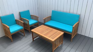 Een houten zitgedeelte buiten, met een bank en twee stoelen, een kleine tafel en een houten terras.
