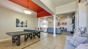 Uma sala de estar ampla com mesa de pingue-pongue, um sofá cinzento e uma mesa de jantar.