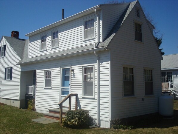 A two-story white house with a front porch, a small front yard, and a visible water tank. - Cozy Cottage at Footbridge Beach - Great Fall and Spring Rates (Ogunquit)