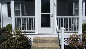 Une maison blanche à deux étages, dotée d’un porche à l’avant, d’une porte portant le numéro 87 et d’un petit escalier menant à l’entrée.