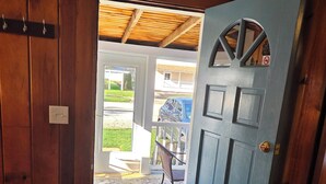 Une porte en bois donnant sur un espace extérieur agrémenté d’un tapis à motifs et d’une chaise.