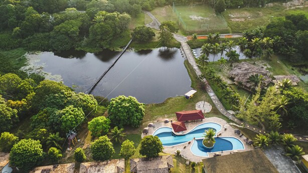 Vue aérienne d’un complexe hôtelier comprenant un grand lac, une piscine et une végétation luxuriante.