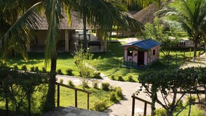 A courtyard with a small pink building, a palm tree, and a pathway leading to a building with a tiled roof. - Rio das Garças Eco Resort (Sao Jose de Mipibu)