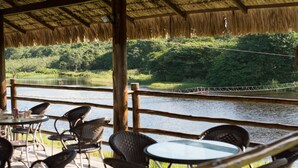 An outdoor seating area with wicker chairs and tables, overlooking a river and lush greenery. - Rio das Garças Eco Resort (Sao Jose de Mipibu)