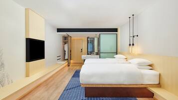 Une chambre d’hôtel moderne dotée d’un grand lit, d’un téléviseur à écran plat fixé au mur et d’un petit coin salon avec un banc.