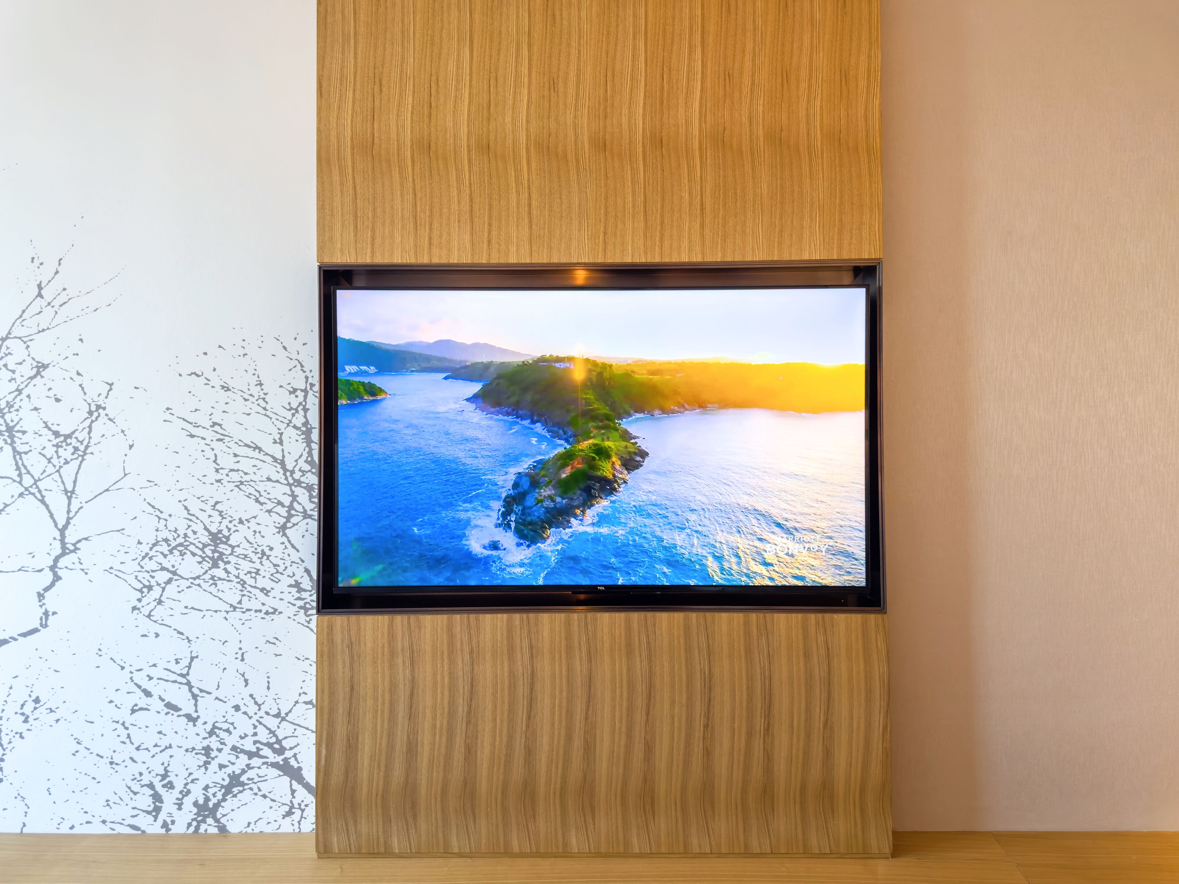 En platt-TV monterad på en väggpanel av trä, som visar ett vackert kustlandskap.