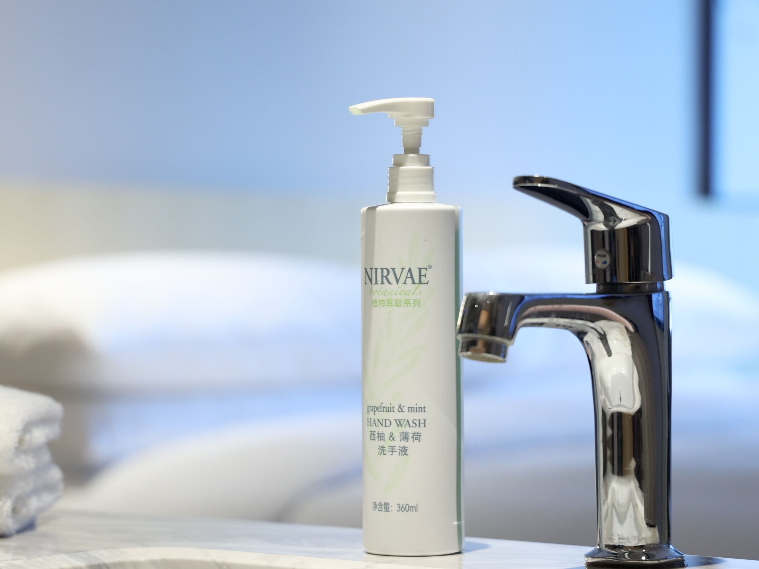 Eine Handseifenflasche mit dem Aufdruck 'NIRVAE' neben einem chromfarbenen Wasserhahn auf einer Badezimmerarbeitsfläche.