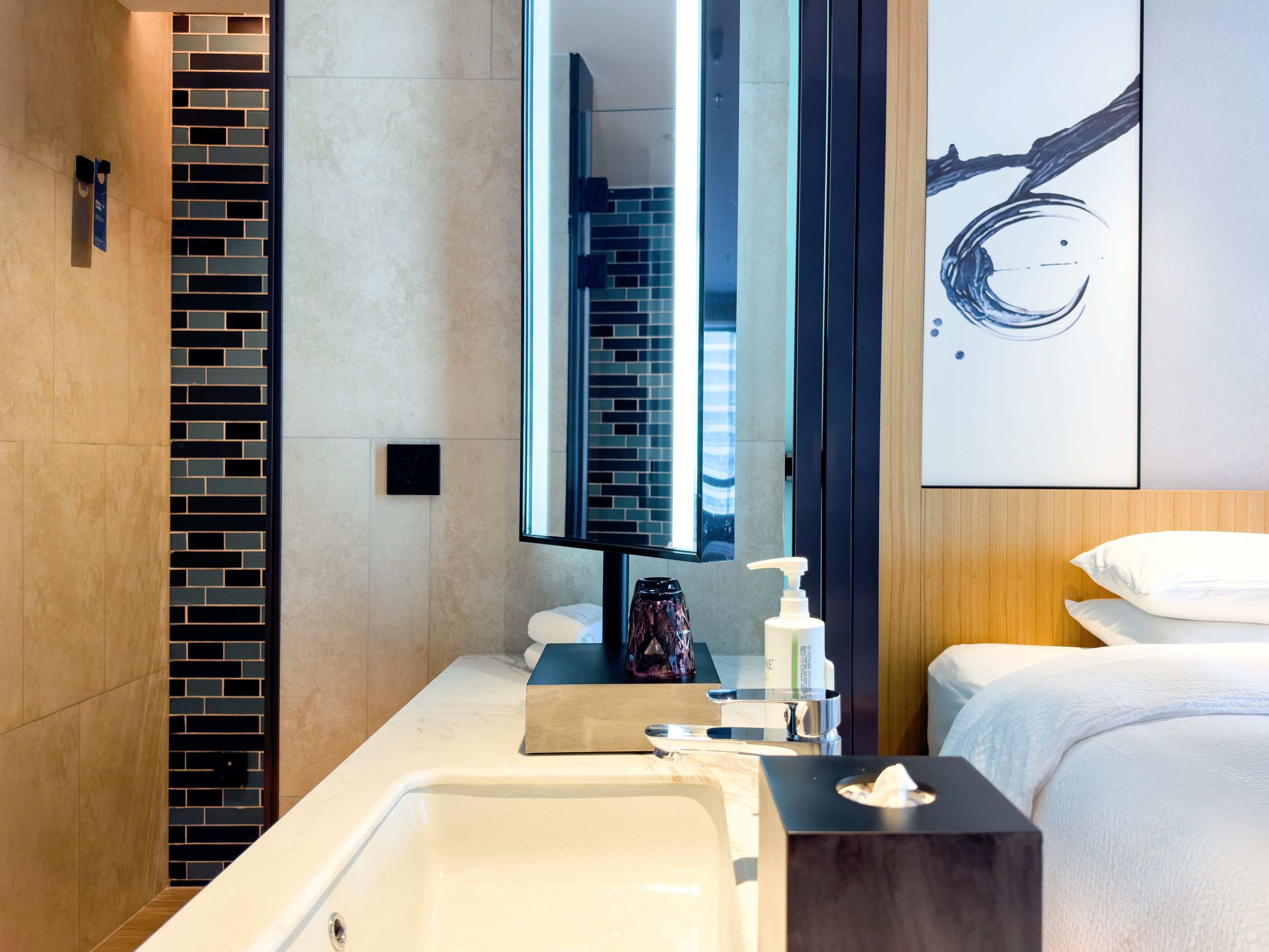 Un baño moderno con un espejo grande, una bañera, un lavamanos y una cama con ropa blanca.