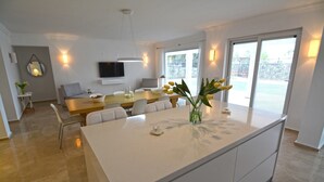 A modern kitchen with a central island, a dining area with chairs, and a TV mounted on the wall. - 5 bedroom luxury villa with private pool and garden in oludeniz (Fethiye)