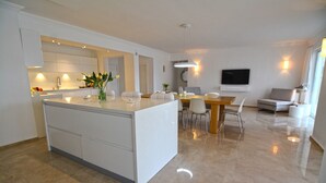 A modern kitchen with a central island, a dining area with a wooden table and chairs, a flat-screen TV mounted on the wall, and a grey sofa in the living area. - 5 bedroom luxury villa with private pool and garden in oludeniz (Fethiye)