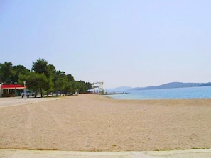 A beach with a clear sky, a few trees, and a distant view of mountains. - Apartments Kristina (Vodice)