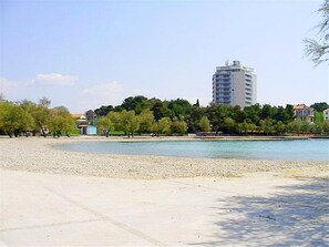 A beach with a clear sky, a few trees, and a tall building in the background.